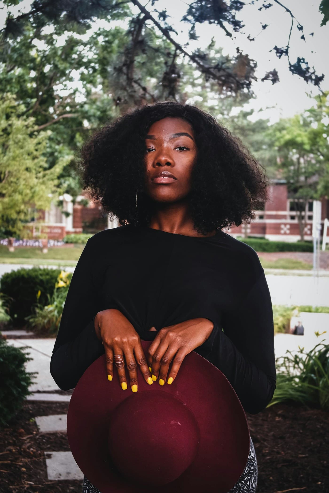 Woman with an afro and yellow nails holding a burgundy hat