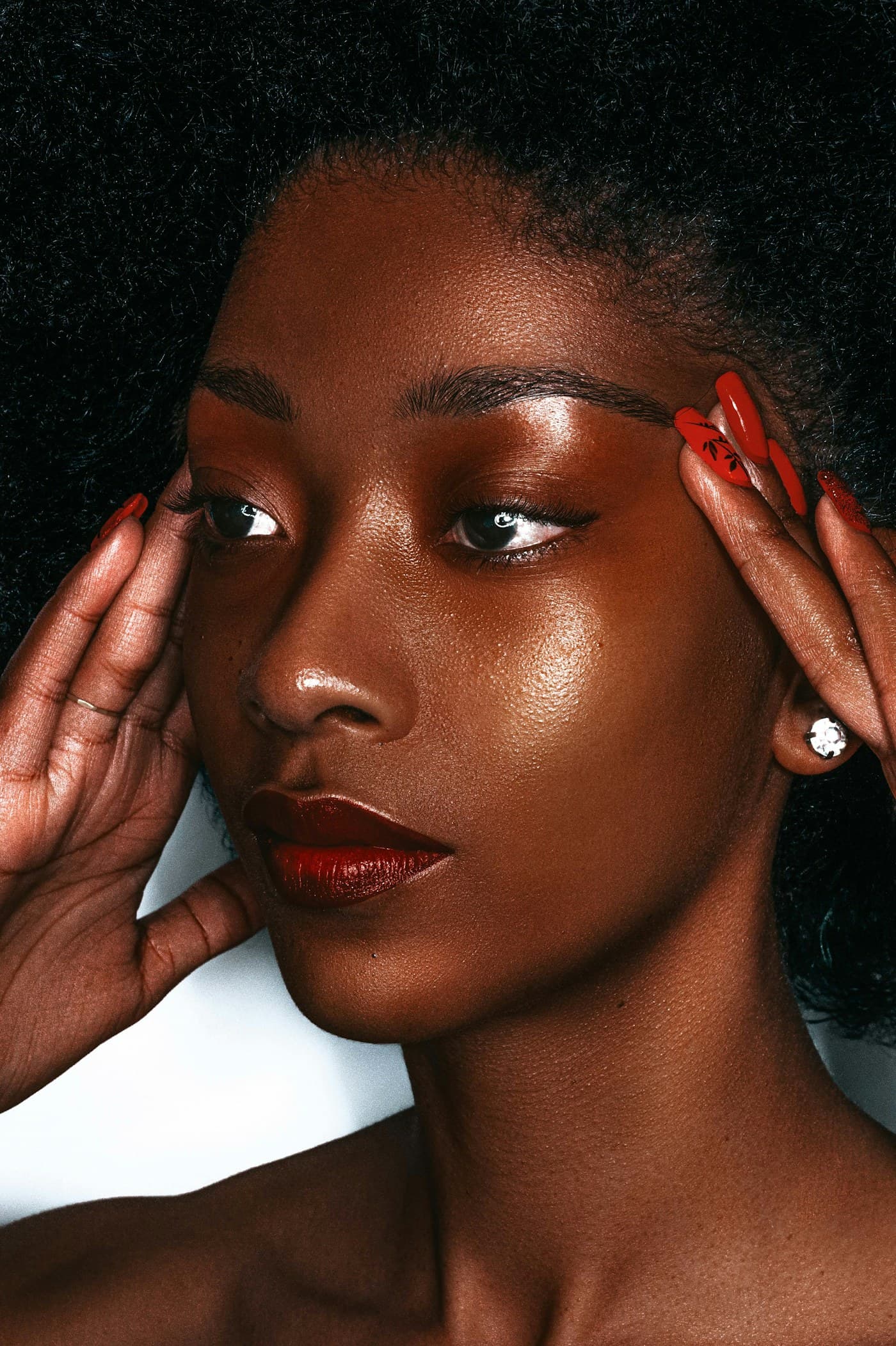 Woman with glossy skin and red nails framing her face