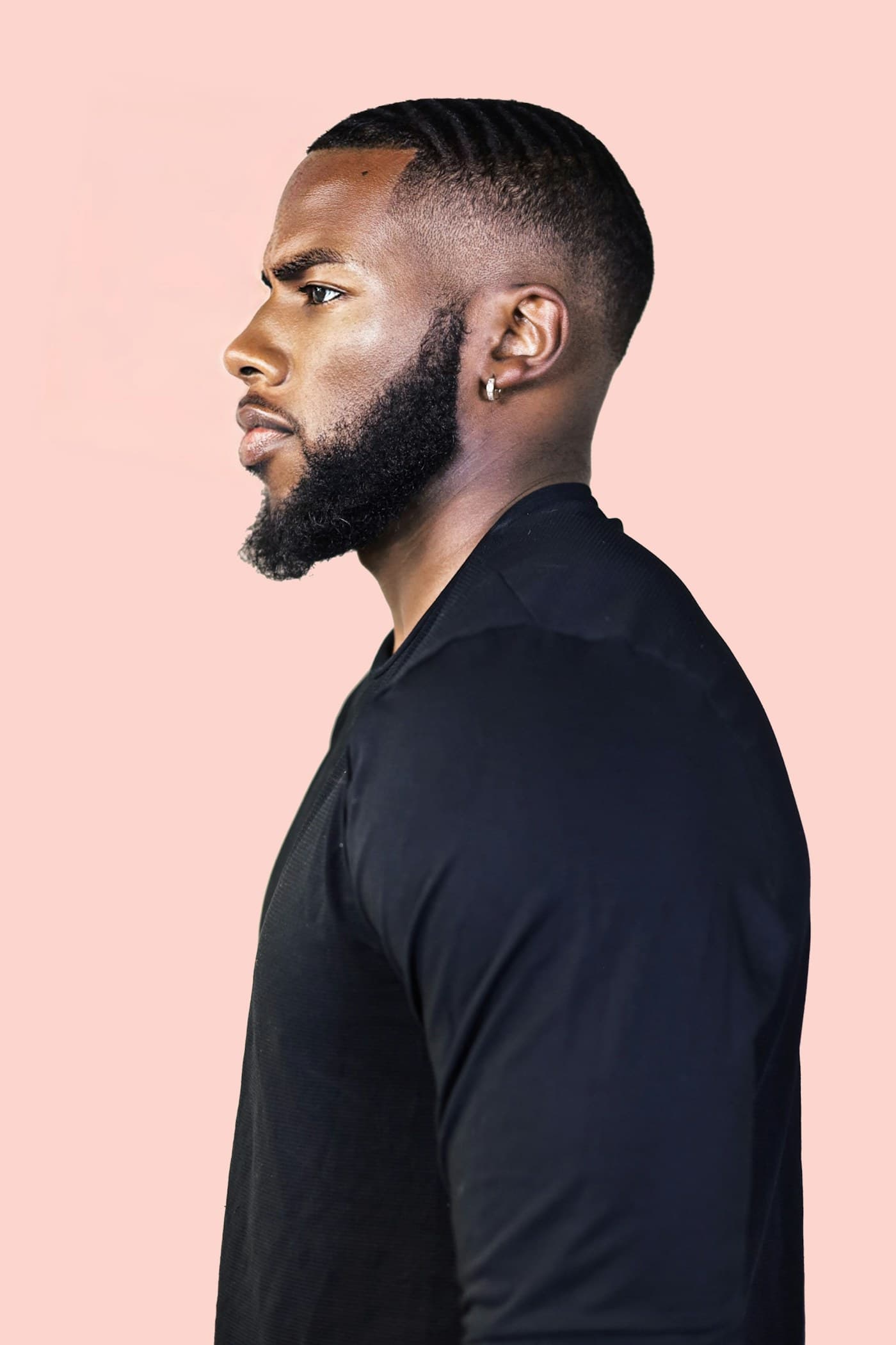 Man with a sculpted beard in profile against a pink wall